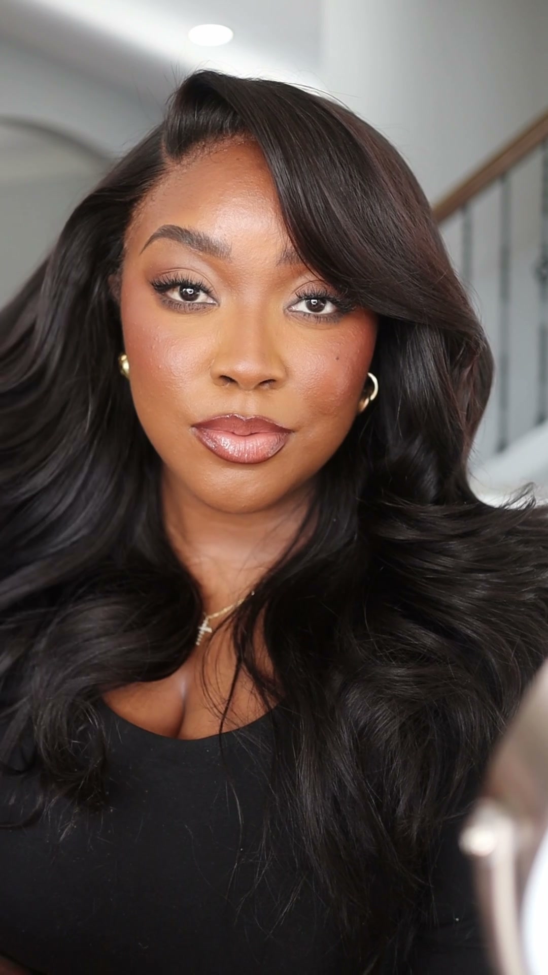 Jaslyn Page looking toward the camera in a simple black top, with warm finished makeup and softly waved hair