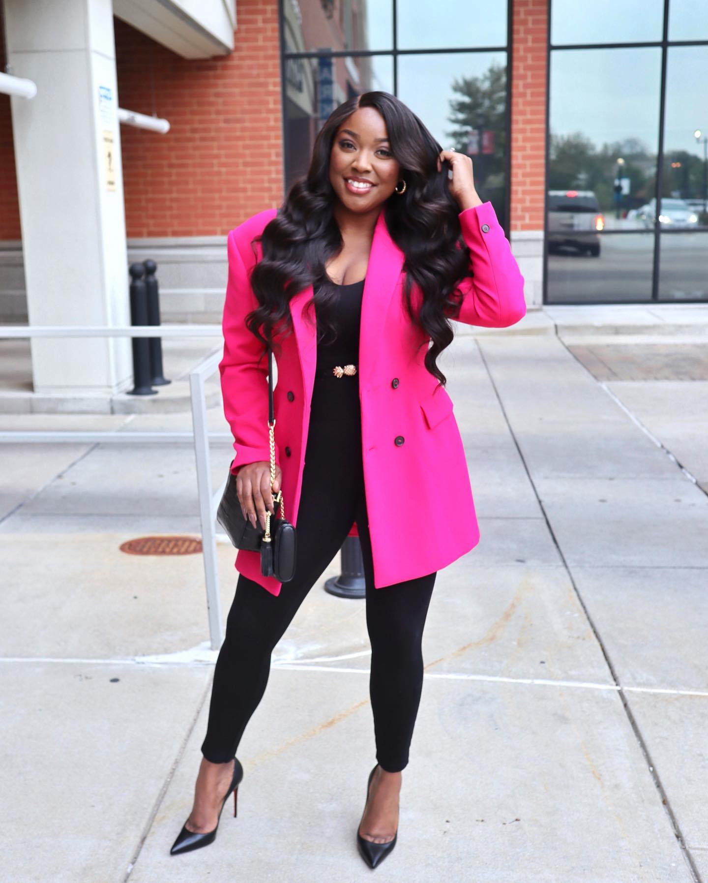 Jaslyn smiling outdoors in a bright pink blazer with a black outfit and heels